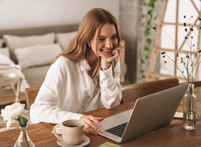 woman smiles while surfing the web on laptop, working from home