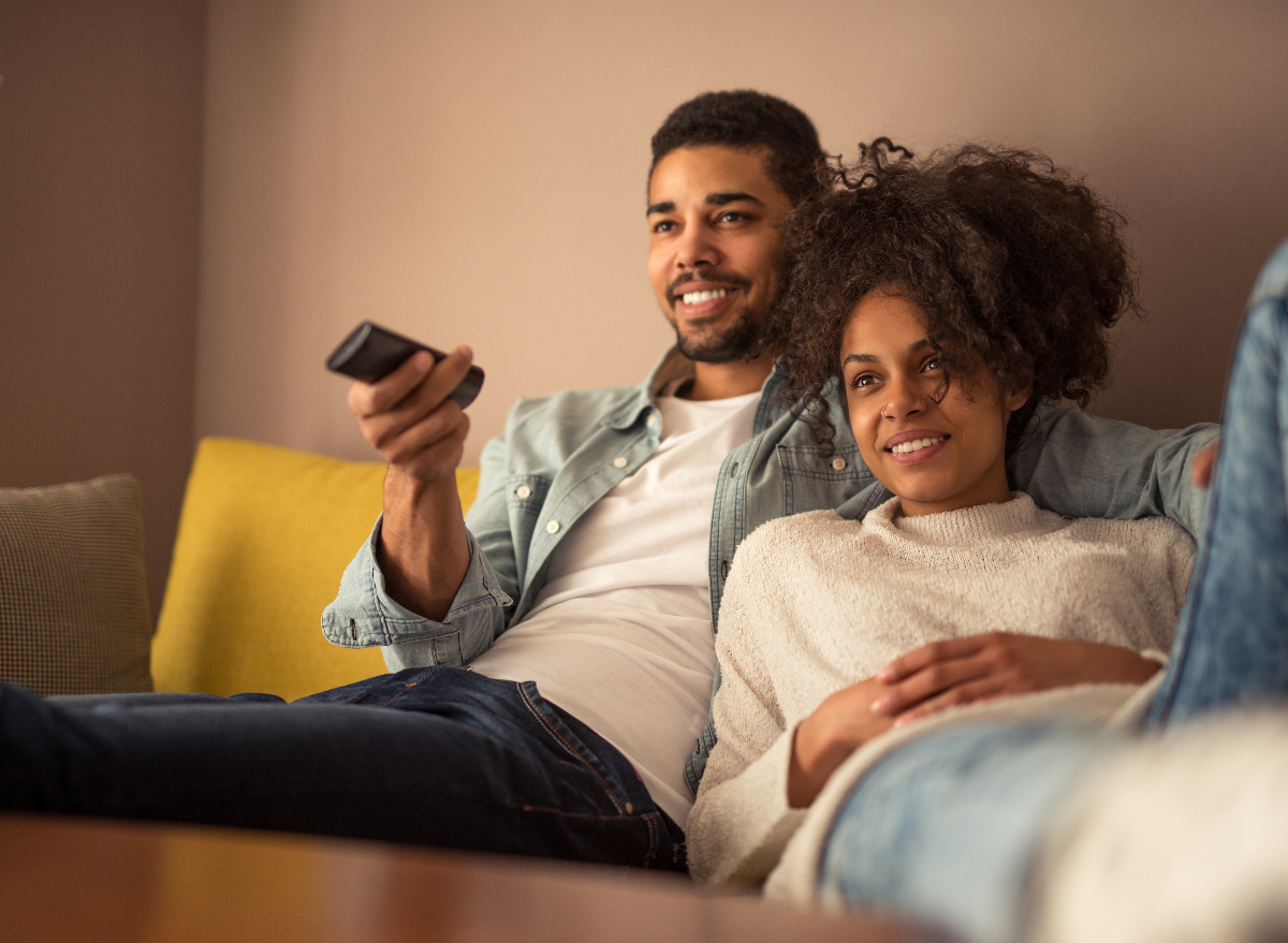 happy, young couple cuddled up watching TV on couch