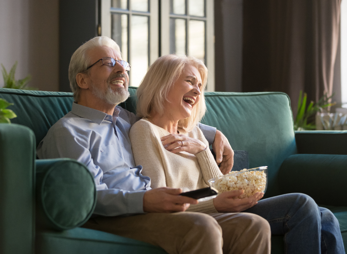 older couple laughing while watching TV and enjoying popcorn