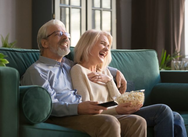 older couple laughing while watching TV and enjoying popcorn