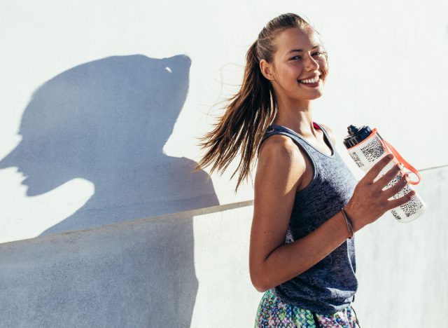 happy woman in workout clothes holding water bottle