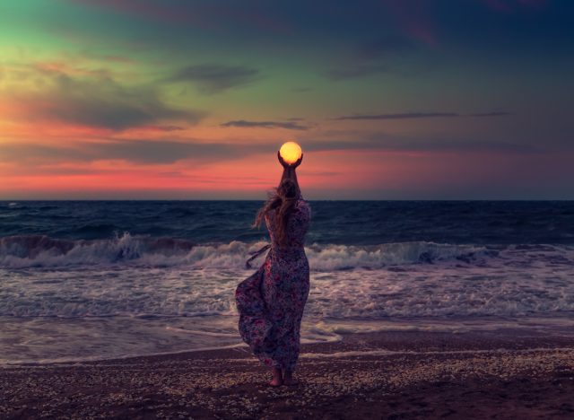 a woman holding the moon on the beach