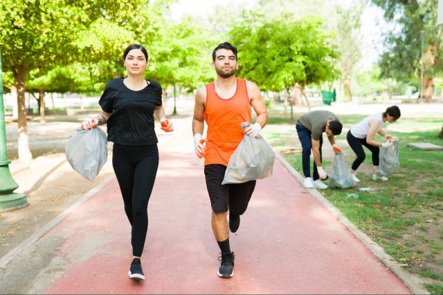 couple jogging while holding bags of trash