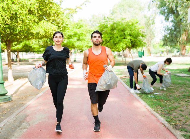 couple jogging while holding bags of trash