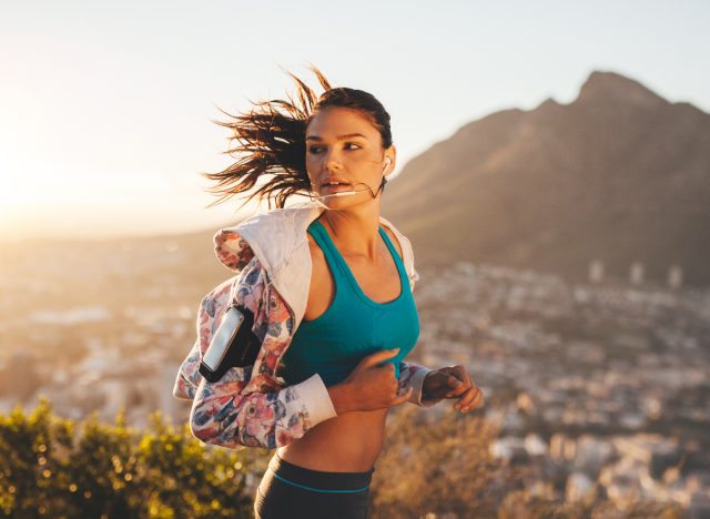 woman jogs at sunset on hill overlooking city