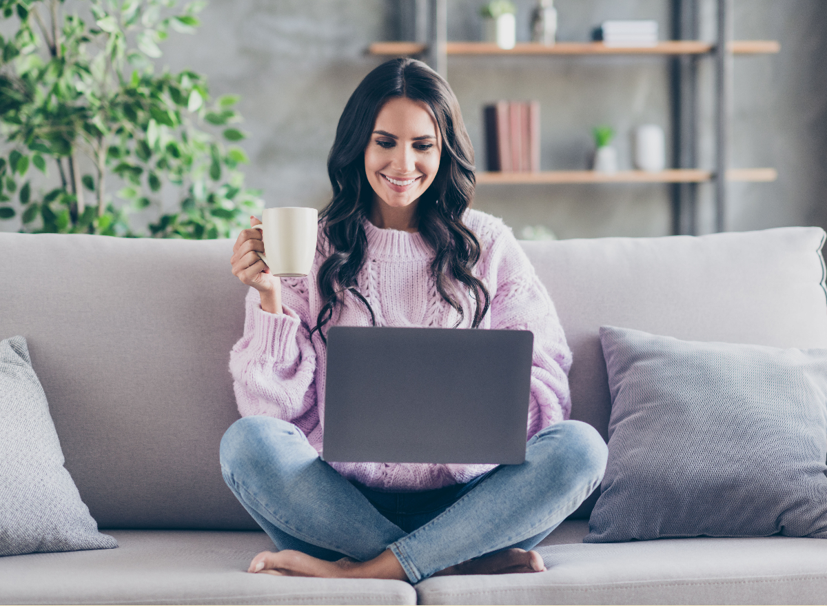 woman in purple sweater sits on couch while watching virtual event on laptop