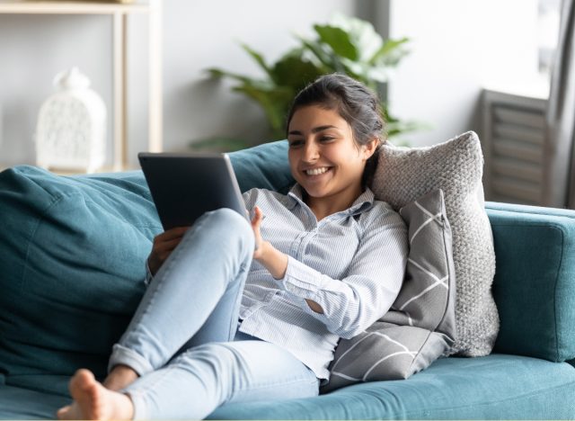 woman relaxed and happy on couch while viewing virtual event on tablet