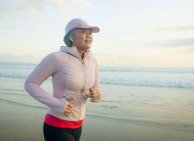 woman over 40 dressed in pink hat and jacket runs on beach