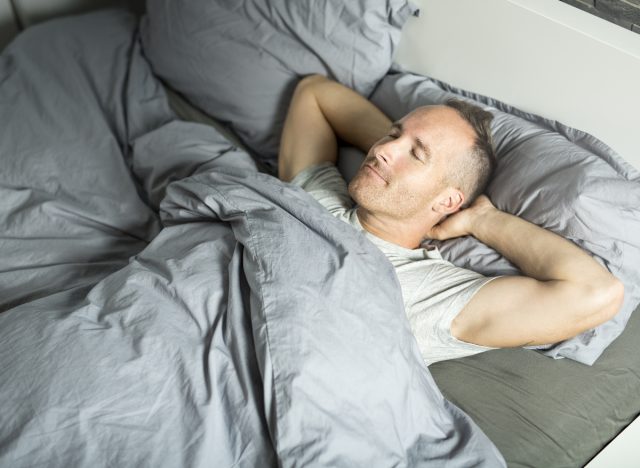 man sleeps restfully on his back in bed