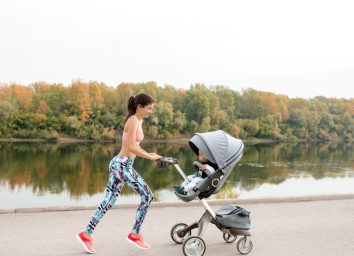 woman in athletic attire jogging with her baby in a stroller along lake