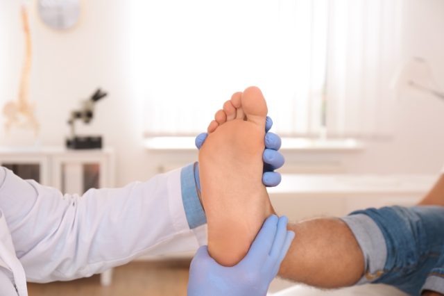 Male orthopedist checking patient's foot in clinic.