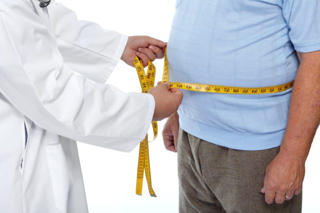 Doctor measuring obese man's body fat at waist.