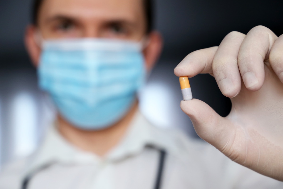 Doctor in medical mask holding medication in capsule.