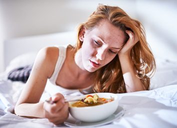 woman eating on the bed while feeling sick