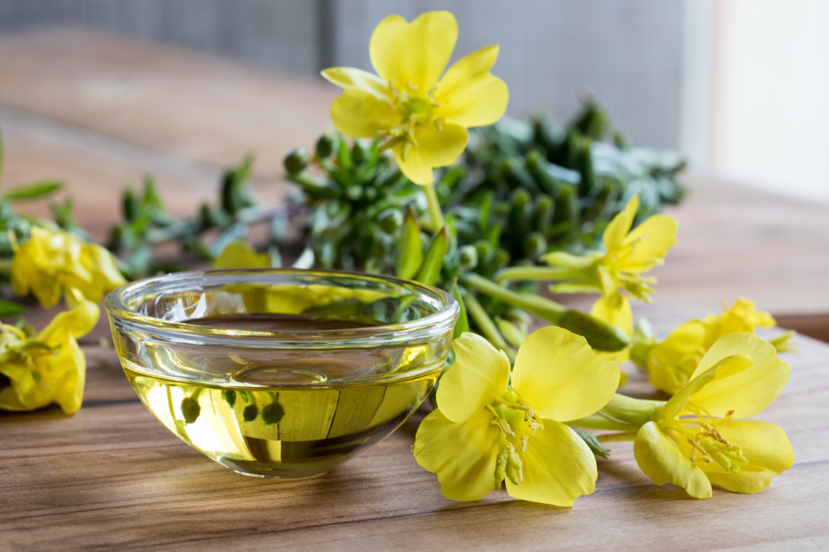 Evening primrose oil in a glass bowl, with fresh evening primrose flowers in the background.