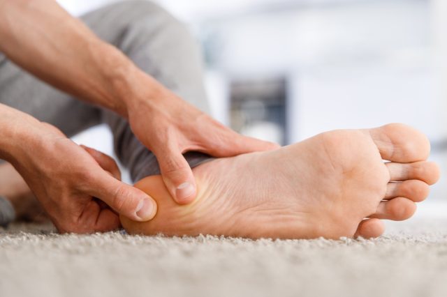 Man hands giving foot massage to yourself after a long walk, suffering from pain in heel spur.