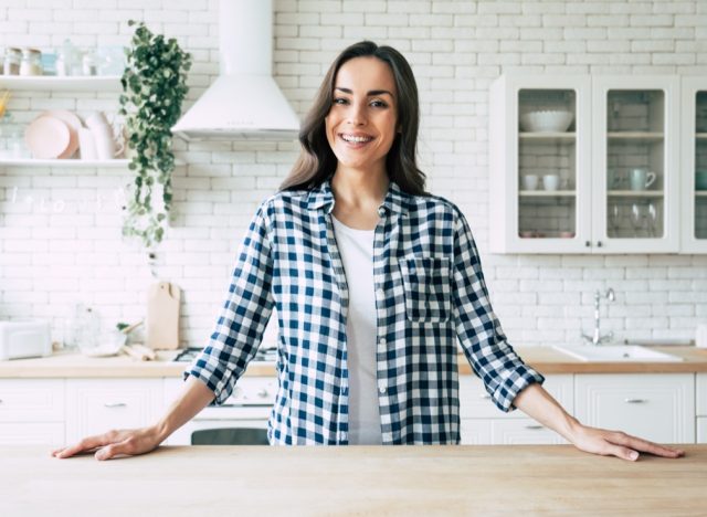 Young smiling woman stands near table on kitchen at home.