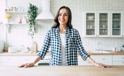 Young smiling woman stands near table on kitchen at home.