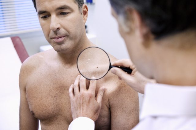 Dermatologist checking skin on male patient chest.