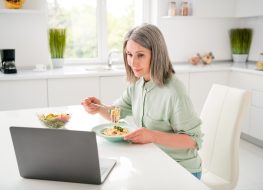 Portrait of attractive focused grey-haired woman eating homemade dinner watching video at home light white indoors