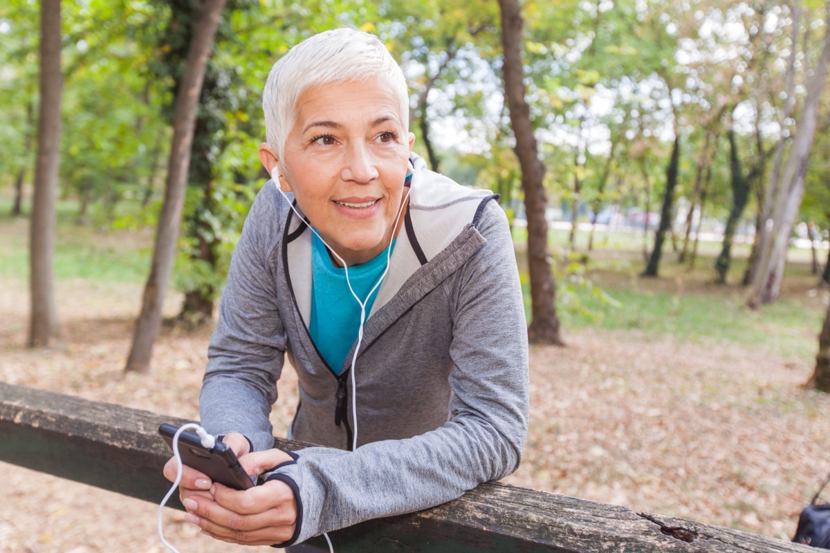 Senior Woman Relax Listening Music With Phone After Jogging In Forest. Fit Lifestyle Mature People Workout Outdoor.