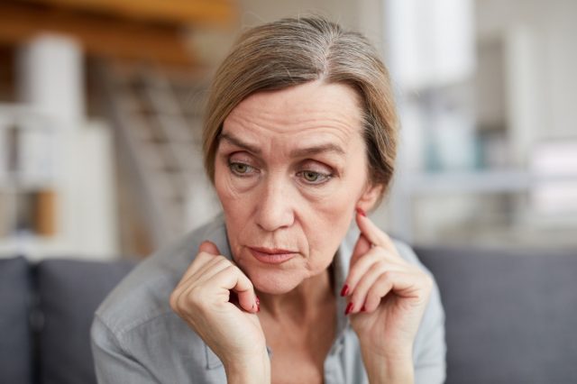 Retrato de una triste mujer madura sentada en el sofá de casa y mirando hacia otro lado con preocupación y ansiedad.