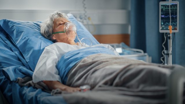 Ältere Frau mit Sauerstoffmaske, die im Krankenhausbett schläft