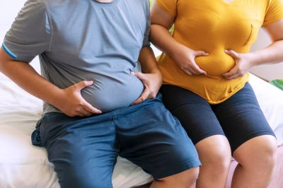 Man and woman holding their bellies while sitting on the bed suffering from extra weight.