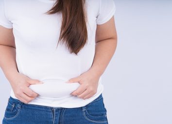Close up woman holding excessive belly fat, overweight abdomen on white background