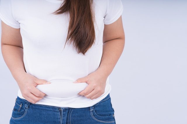 Close up woman holding excessive belly fat, overweight abdomen on white background