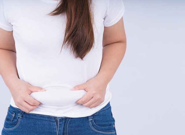 Close up woman holding excessive belly fat, overweight abdomen on white background
