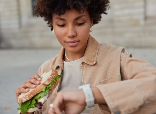 woman eating sandwich and checking watch