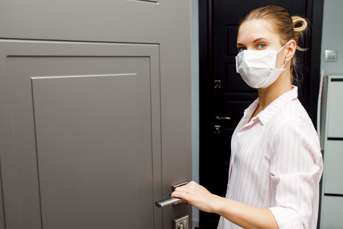 Young woman in medical mask opening door.