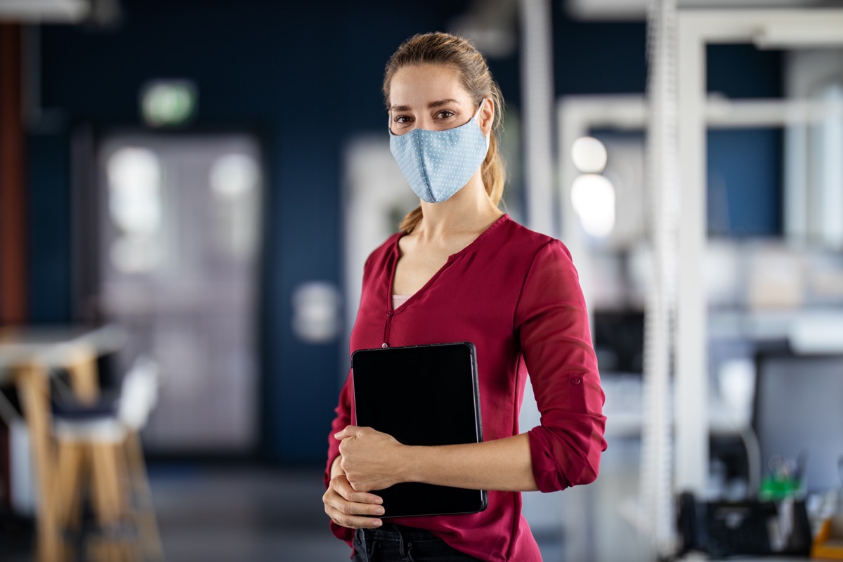 Portrait of a young businesswoman with face mask standing in office holding a digital tablet