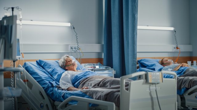 Elderly woman wearing oxygen mask sleeping in hospital bed.