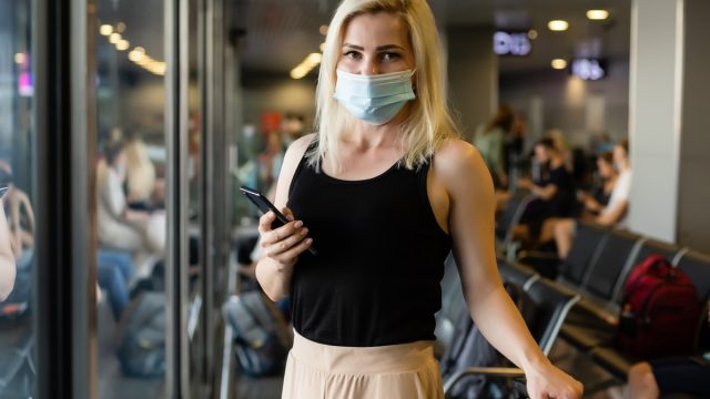 Woman walking with surgical mask face protection walking in crowds at airport station.