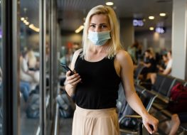 Woman walking with surgical mask face protection walking in crowds at airport station.