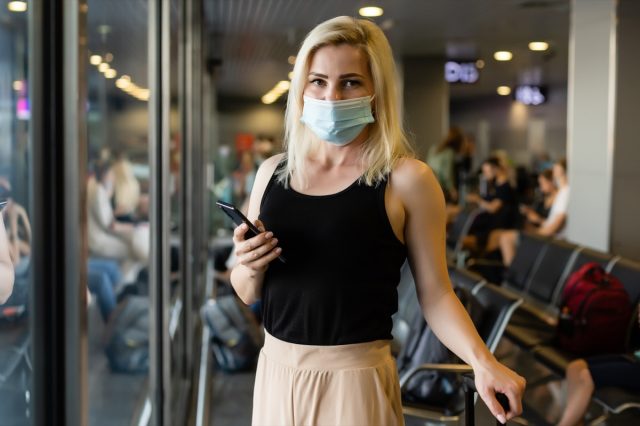 Woman walking in surgical mask face shield walking in crowds at airport train station.