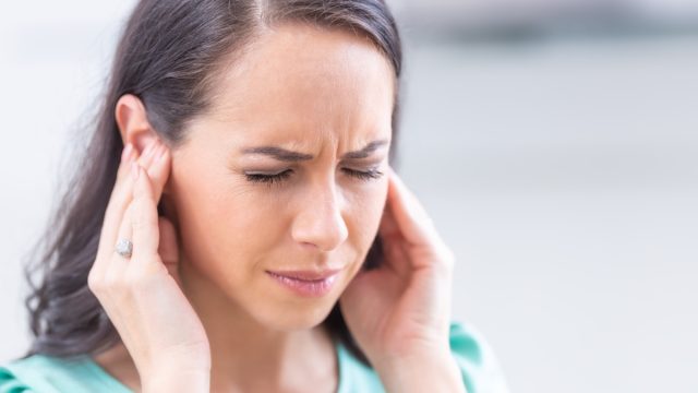 Young woman have headache migraine stress or tinnitus - noise whistling in her ears.