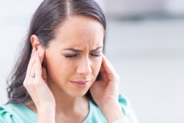 A young woman has a headache, migraine stress or tinnitus - a ringing noise in her ears.