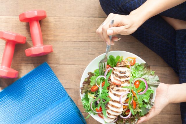 woman with chicken salad, dumbbells and yoga mat