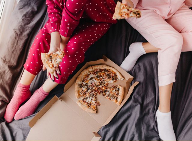 two women in PJs eating pizza in bed