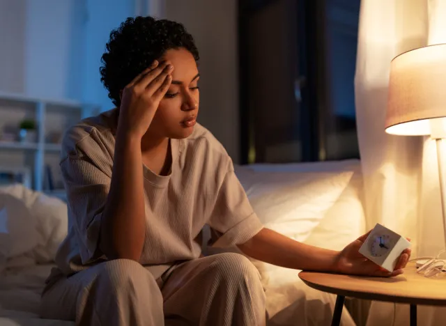 woman looking stressed at alarm clock when waking up in the middle of the night