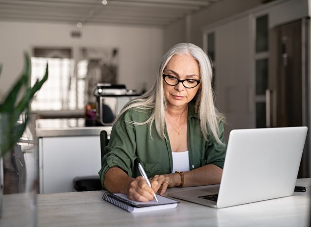 woman works at home desk with laptop and notepad