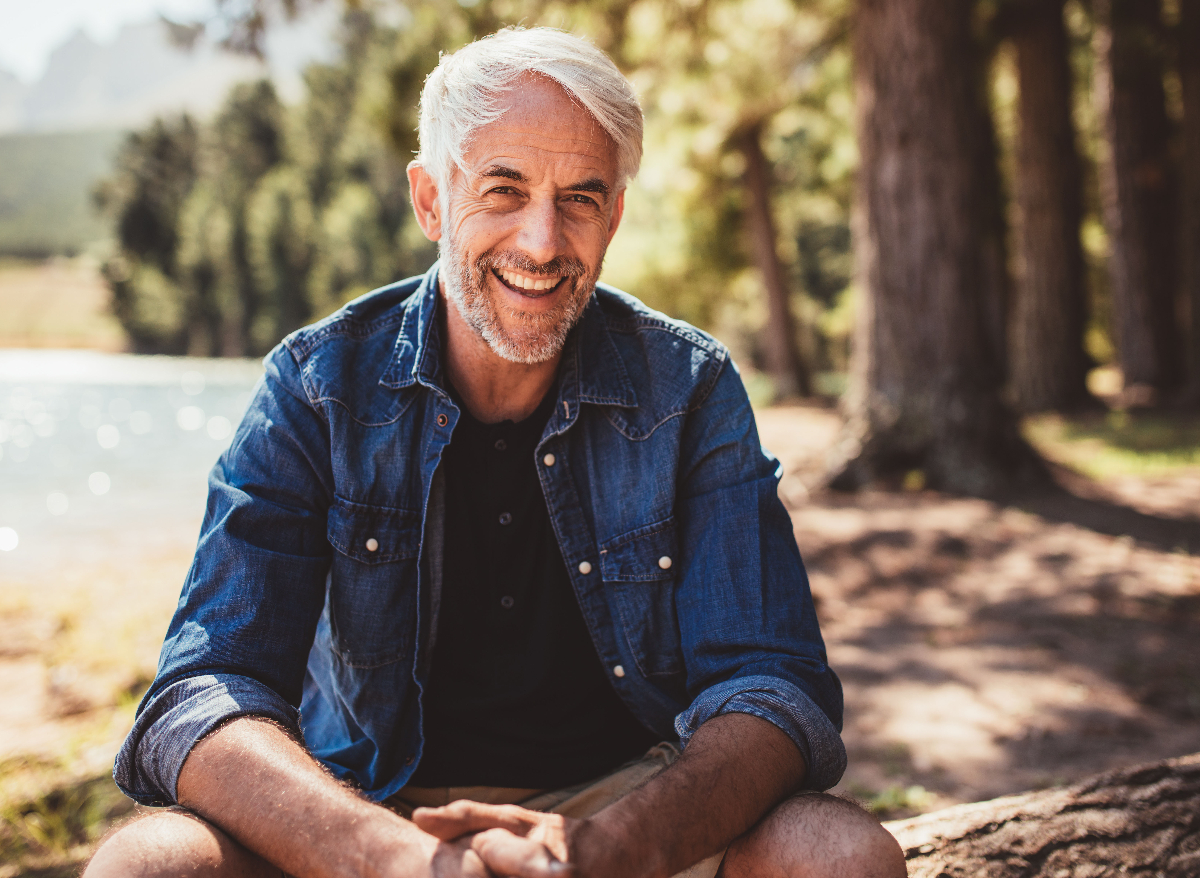 happy man wearing denim button-down sits outdoors