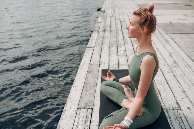 woman relaxes while doing yoga by the water