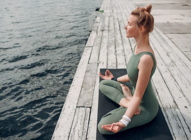 woman relaxes while doing yoga by the water