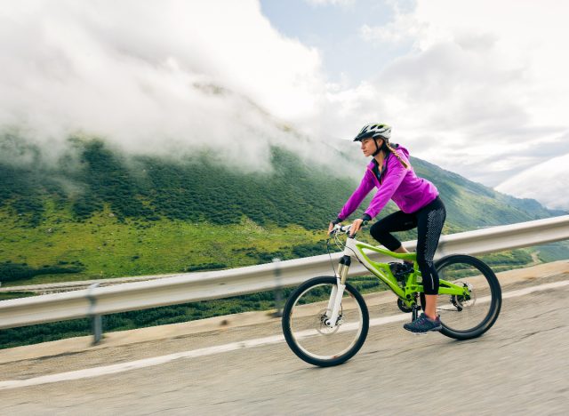 athletic woman bikes down hill with scenic mountain backdrop