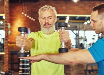 older man does arm exercise with weights and trainer