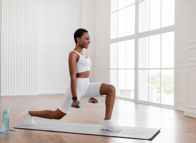 woman lunges on yoga mat with dumbbells